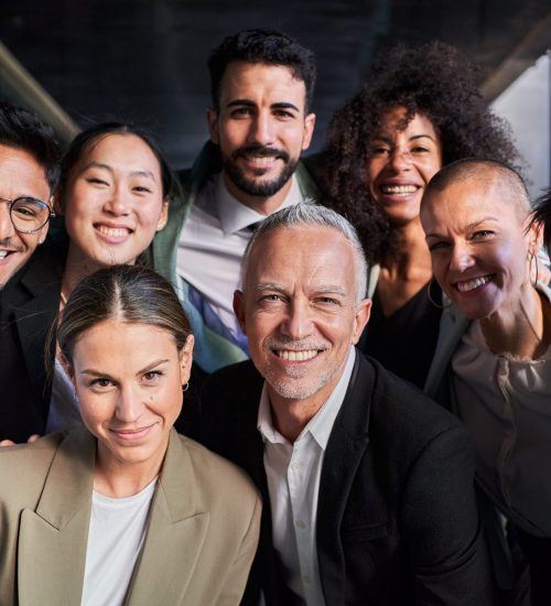 Cheerful portrait of a group of business colleagues taking a photo for the company page in the office, gathered looking at camera smiling, headed by the boss. Startup concept.